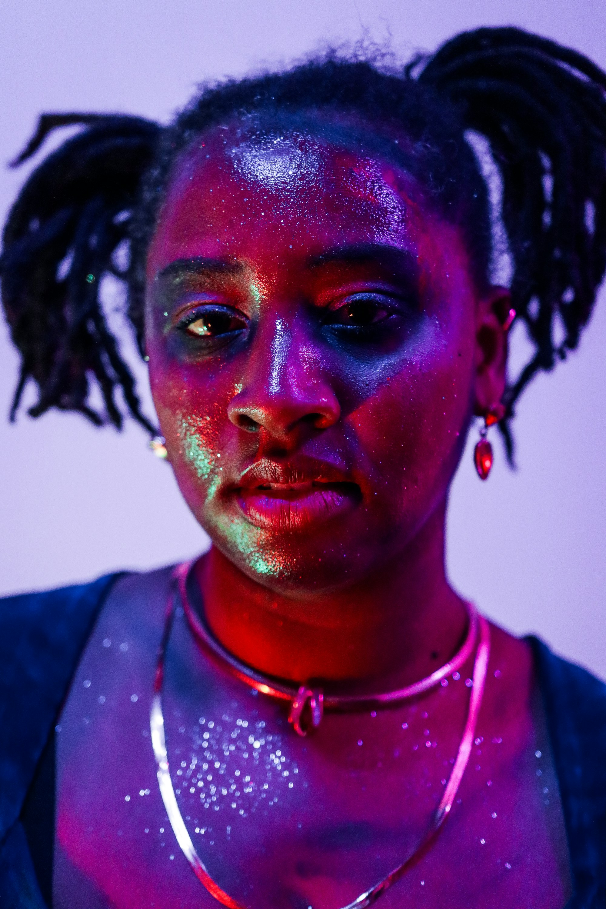 Person with glitter on their face under coloured light